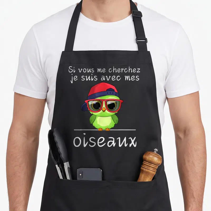 Tablier de cuisine noir avec un hibou vert portant des lunettes rouges et une casquette bleue au centre du motif imprimé.