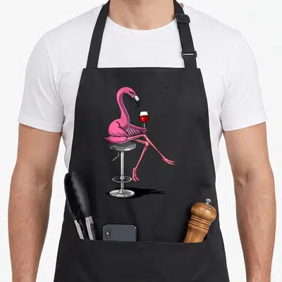 Tablier de cuisine noir avec illustration d'un flamant rose pink assis sur un tabaret tenant un verre de vin rouge.