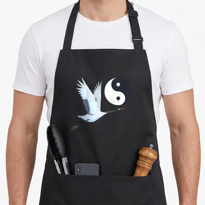 Tablier de cuisine noir avec une grue blanche en vol aux ailes déployées à côté d'un cercle Yin Yang noir et blanc.