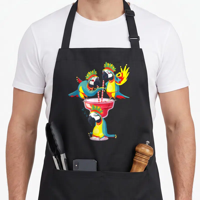 Tablier de cuisine noir avec trois perroquets hawaïens décorés buvant dans un grand verre rose à pailles rouges et blanches.