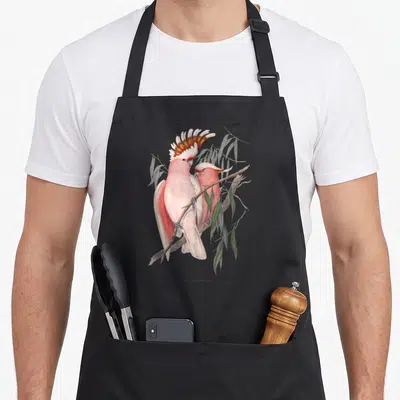 Tablier de cuisine noir avec deux cacatoès roses perchés sur une branche aux feuilles vertes dans un style naturaliste.
