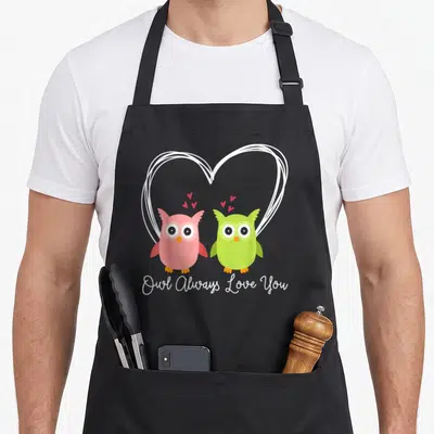 Tablier de cuisine noir avec deux chouettes colorées et un grand cœur blanc dessiné au trait.