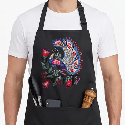 Tablier de cuisine noir avec un grand oiseau stylisé aux couleurs vives entouré de fleurs et de feuilles dans un style folklorique.