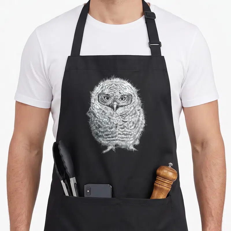 Tablier de cuisine noir avec illustration détaillée d'un jeune hibou Screech aux yeux ronds et plumage texturé.