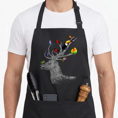 Tablier de cuisine noir avec illustration d'un cerf gris aux bois servant de perchoir à des oiseaux tropicaux multicolores.