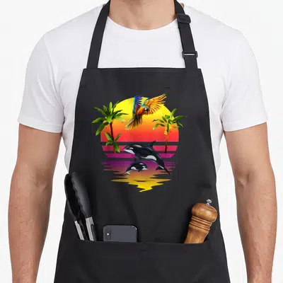 Tablier de cuisine noir avec un perroquet coloré en vol et deux orques sautant devant un soleil couchant entre des palmiers.