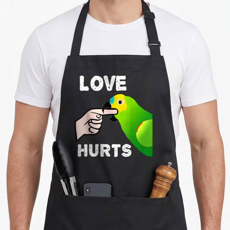 Tablier de cuisine noir avec illustration colorée d'un perroquet vert pincant un doigt sous le texte Love Hurts en blanc.