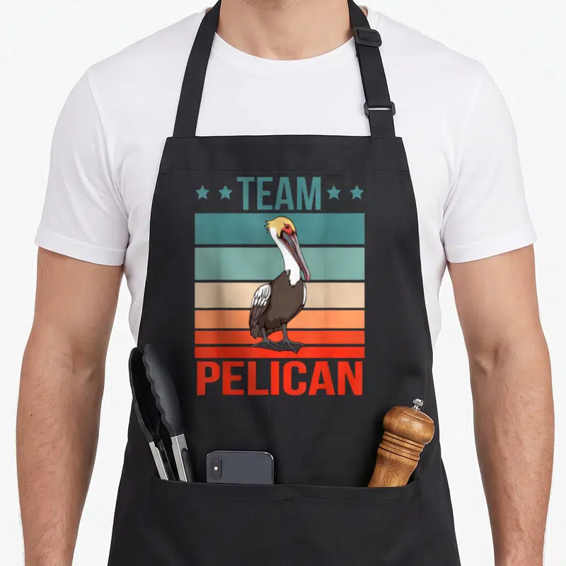 Tablier de cuisine noir avec illustration d'un pélican aux couleurs rétro et texte Team Pélican en haut et bas du motif.