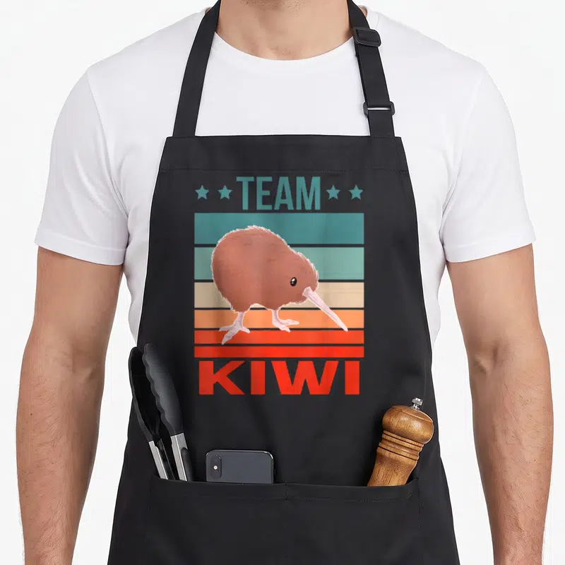 Tablier de cuisine noir avec illustration d'un kiwi brun sur fond de bandes horizontales colorées et texte Team Kiwi.