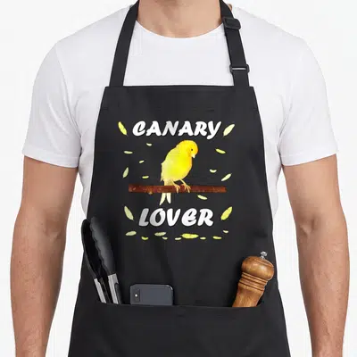 Tablier de cuisine noir avec un canari jaune sur une branche et le texte « canary lover » entouré de plumes jaunes.
