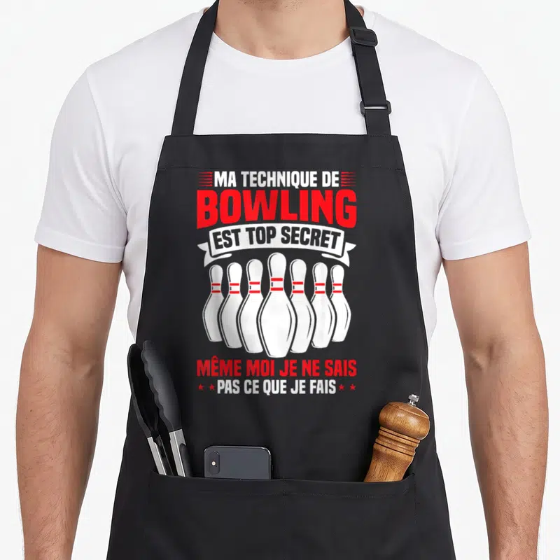 Tablier de cuisine noir avec illustration de quilles de bowling et texte humoristique en rouge et blanc.
