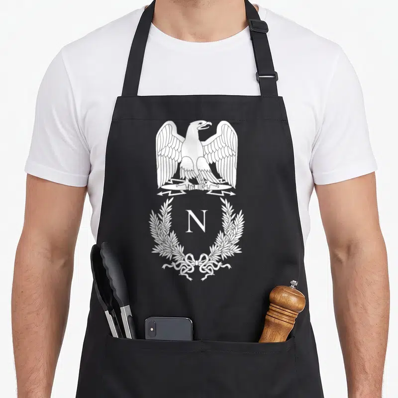 Tablier de cuisine noir avec un aigle aux ailes déployées, une couronne de lauriers et la lettre N au centre.