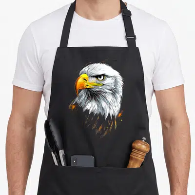 Tablier de cuisine noir avec tête d'aigle royal pygargue au bec jaune et plumes blanches détaillées.
