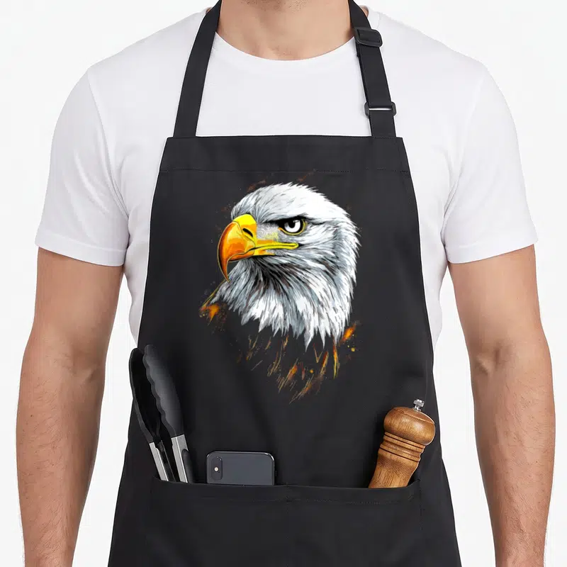Tablier de cuisine noir avec tête d'aigle royal pygargue au bec jaune et plumes blanches détaillées.