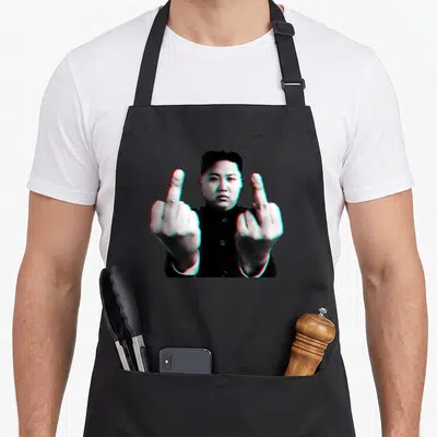 Tablier de cuisine noir avec une illustration de Kim Jong Un levant les deux en style glitch.