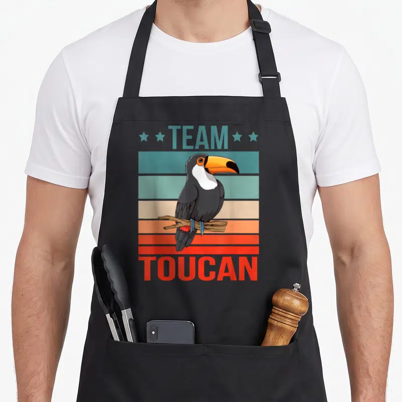Tablier de cuisine noir avec illustration colorée d'un toucan posé sur une branche devant des bandes horizontales vintage.