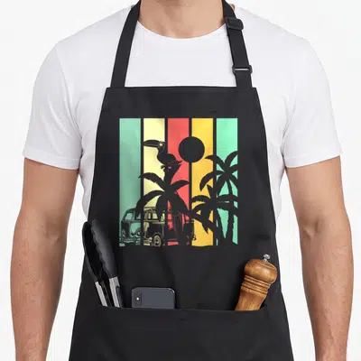 Tablier de cuisine noir avec illustration colorée d'un toucan, de palmiers et d'un van retro sur fond rayé.