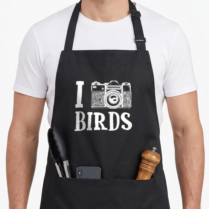 Tablier de cuisine noir avec inscription I BIRDS et dessin d'appareil photo blanc au centre.