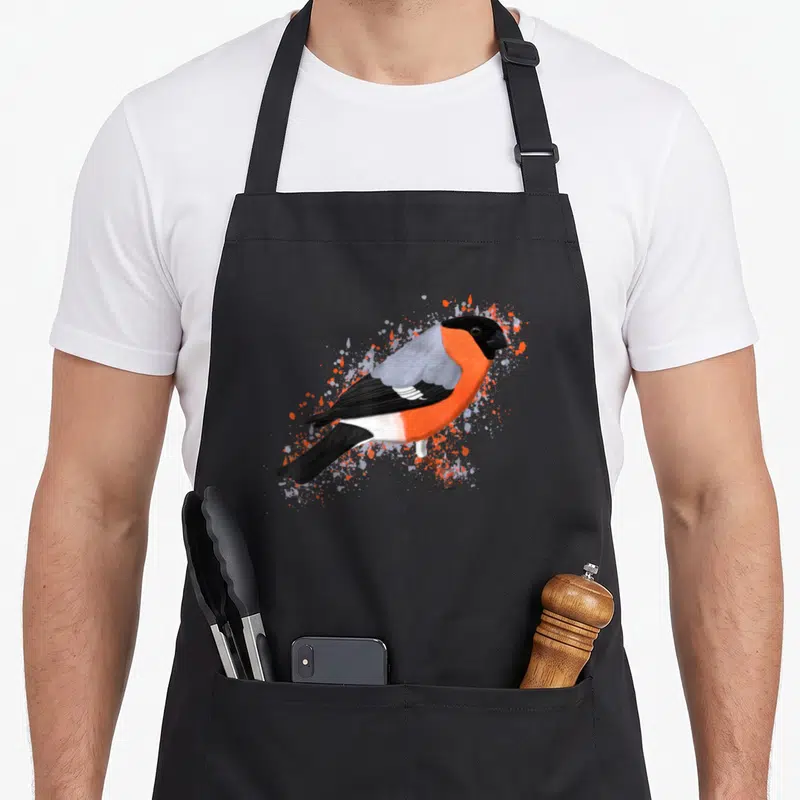 Tablier de cuisine noir avec illustration colorée d'un bouvreuil rouge et gris entouré d'éclaboussures artistiques.