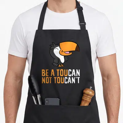 Tablier de cuisine noir avec un toucan cartoon orange et blanc et un jeu de mots en anglais.
