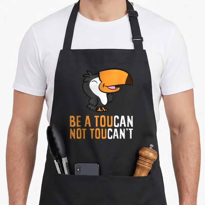 Tablier de cuisine noir avec un toucan cartoon orange et blanc et un jeu de mots en anglais.