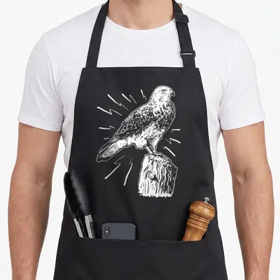 Tablier de cuisine noir avec illustration blanche d'un épervier perché sur un tronc d'arbre en style gravure.