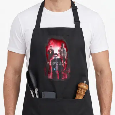 Tablier de cuisine noir avec illustration trois personnages et texte blanc sur fond rouge fumant.
