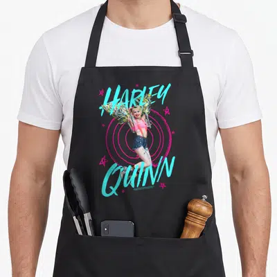 Tablier de cuisine noir avec Harley Quinn aux ailes d'oiseaux et texte turquoise sur fond de cibles roses.