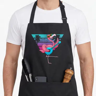 Tablier de cuisine noir avec un flamant rose jouant d'une guitare bleue devant un décor géométrique tropical.