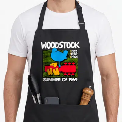Tablier de cuisine noir avec un oiseau bleu posé sur une guitare rouge et le texte Woodstock Summer of 1969 imprimé en blanc.