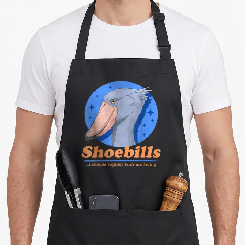 Tablier de cuisine noir avec illustration d'un Shoebill et le texte Shoebills because regular birds are boring en orange.
