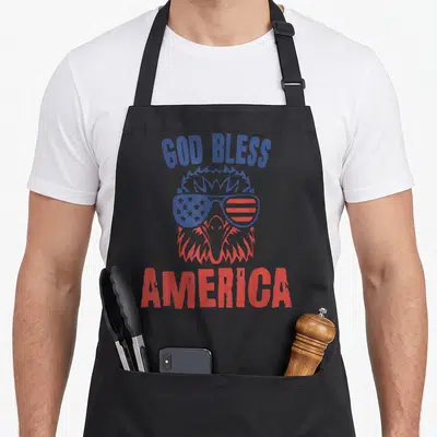 Tablier de cuisine noir avec un aigle portant des lunettes au motif du drapeau américain et le texte God Bless America.