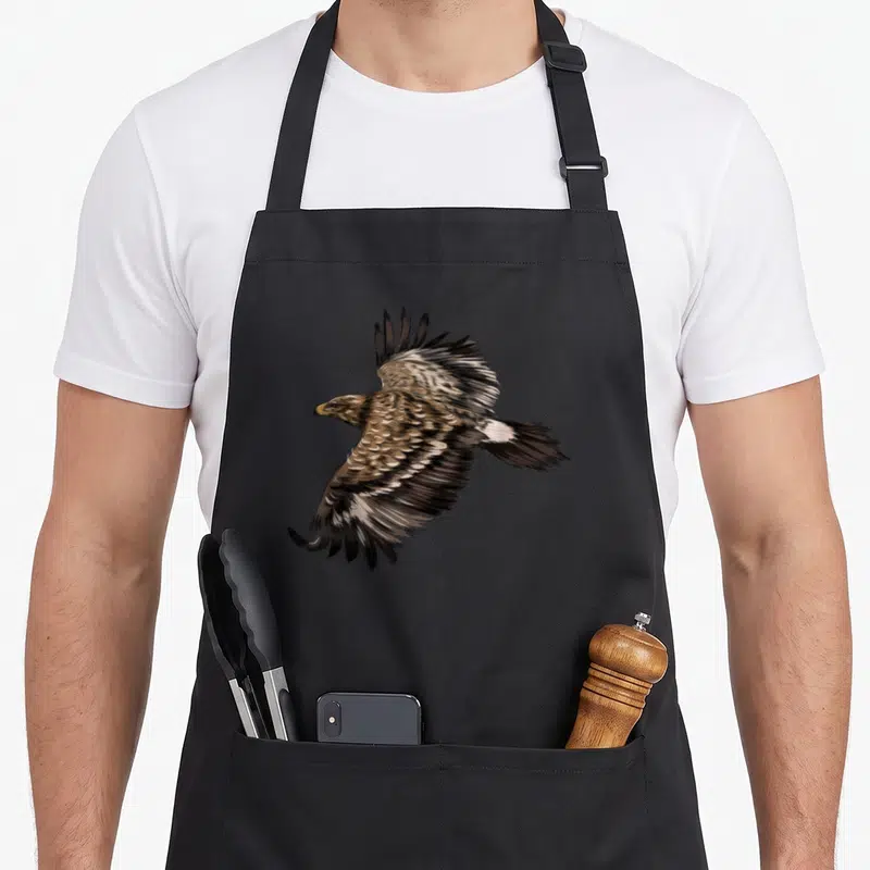 Tablier de cuisine noir avec un aigle aux ailes déployées et des plumes détaillées en vol.