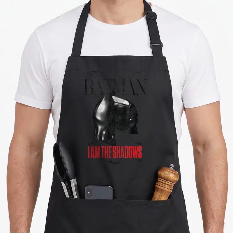Tablier de cuisine noir avec le masque de Batman et le texte I am the shadows en rouge.