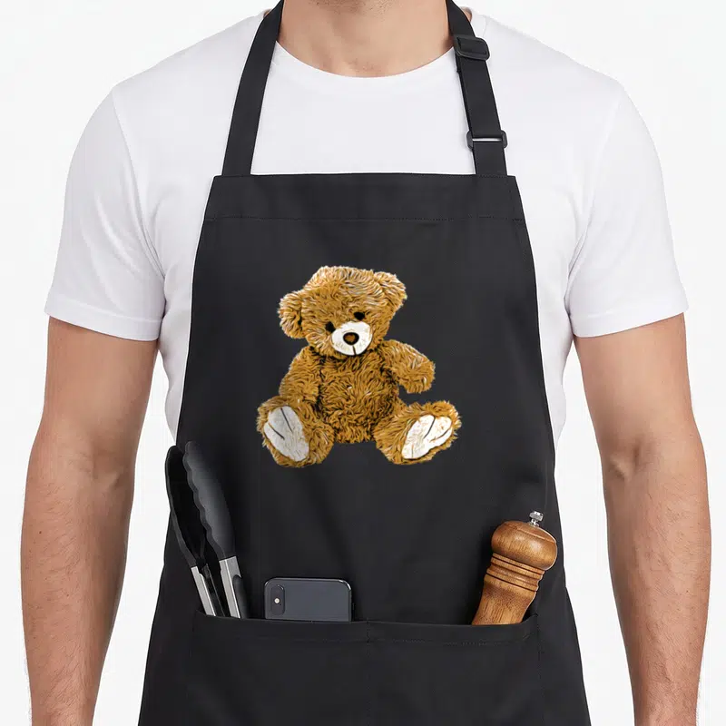 Tablier de cuisine noir avec illustration d'un ours en peluche marron aux pattes blanches assis face à l'utilisateur.