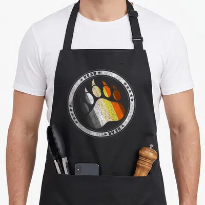 Tablier de cuisine noir avec une patte d'ours multicolore dans un cercle blanc texturé portant le mot BEAR.