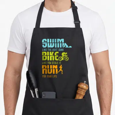 Tablier de cuisine noir avec le texte Swim Like The Boat Sunk, Dine Like You Stole It et Run For Your Life en couleurs vives.