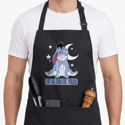 Tablier de cuisine noir avec le Bourriquet de Disney endormi et l'inscription Not A Morning Person sous la lune et les étoiles.
