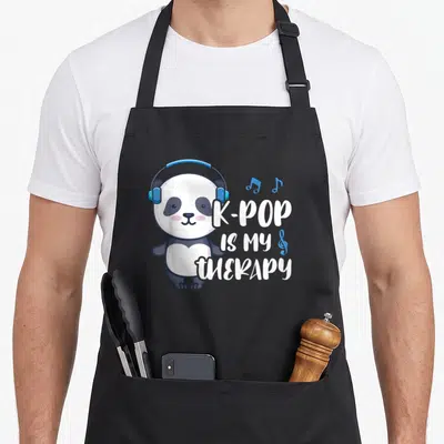 Tablier de cuisine noir avec un panda mignon portant des écouteurs bleus et le texte blanc K-POP IS MY THERAPY entouré de notes de musique.