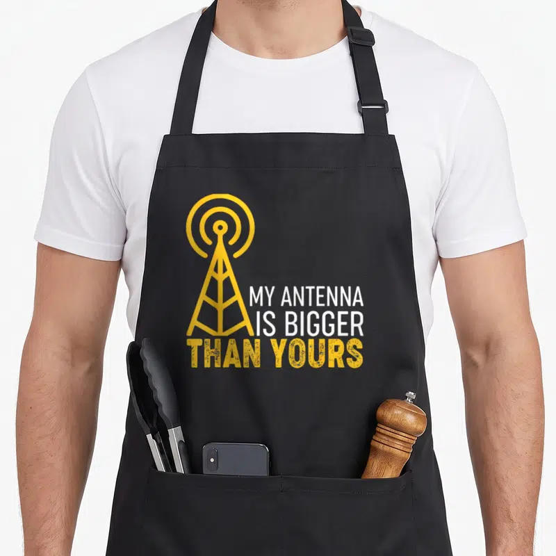 Tablier de cuisine noir avec une antenne radioamateur jaune et le texte My Antenna Is Bigger Than Yours imprimé au centre.