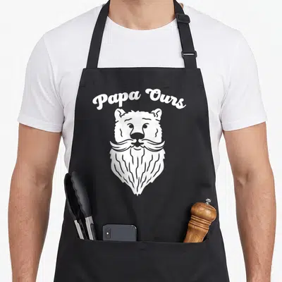 Tablier de cuisine noir avec illustration blanche d'une tête d'ours portant une longue barbe stylisée sous le texte Papa Ours en lettres arrondies.