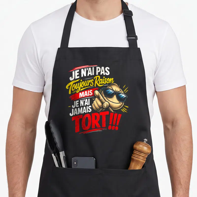 Tablier de cuisine noir avec un smiley aux lunettes bleues pointant l'index et du texte humoristique en blanc, jaune et rouge.