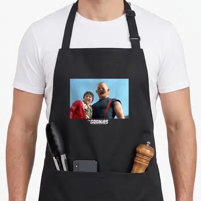 Tablier de cuisine noir avec une illustration de Chunk et Sloth des Goonies sur fond bleu ciel.