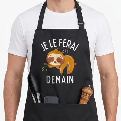 Tablier de cuisine noir avec illustration d'un paresseux dormant et le texte Je le ferai demain en lettres blanches.
