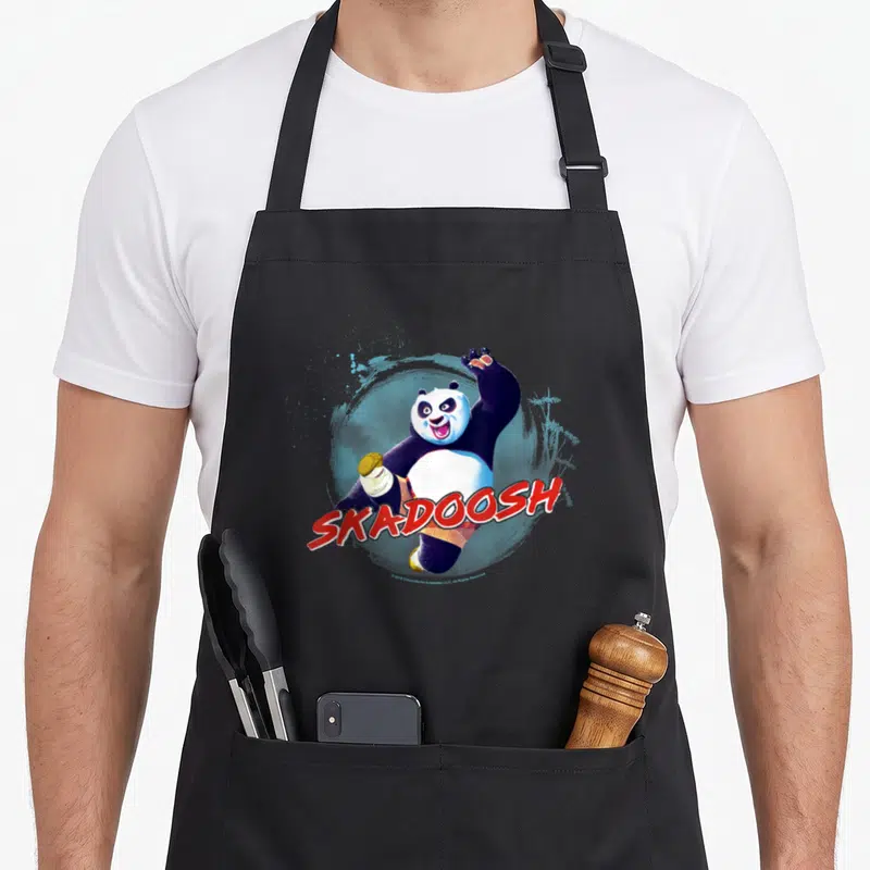 Tablier de cuisine noir avec un panda en pleine action tenant un bol et le texte Skadoosh en rouge.