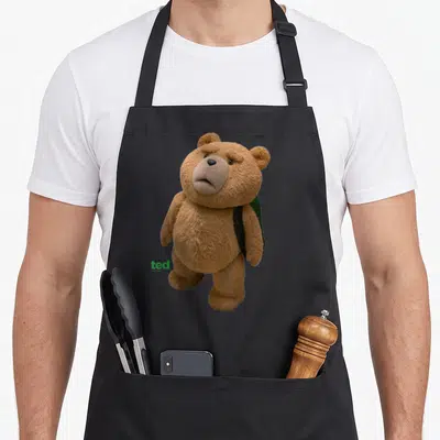 Tablier de cuisine noir avec ours en peluche Ted portant un sac à dos vert et logo vert en bas à gauche.