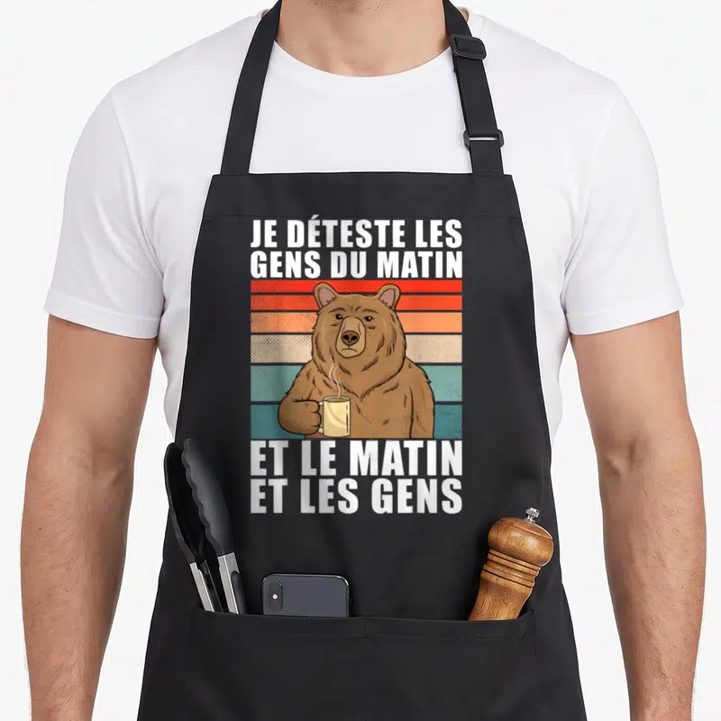 Tablier de cuisine noir orné d'un ours brun tenant une tasse fumante devant des bandes colorées vintage.