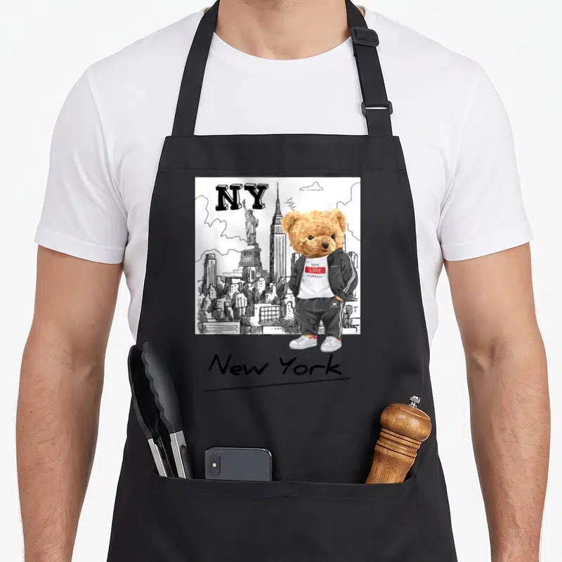 Tablier de cuisine noir avec ours en veste noire devant skyline New York et Statue de la Liberté en dessin au trait.