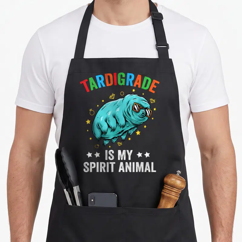 Tablier de cuisine noir avec un tardigrade turquoise en lunettes de soleil et des étoiles dorées.