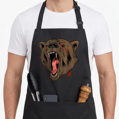 Tablier de cuisine noir avec tête d'ours brun féroce aux griffures rouges et langue pendante.